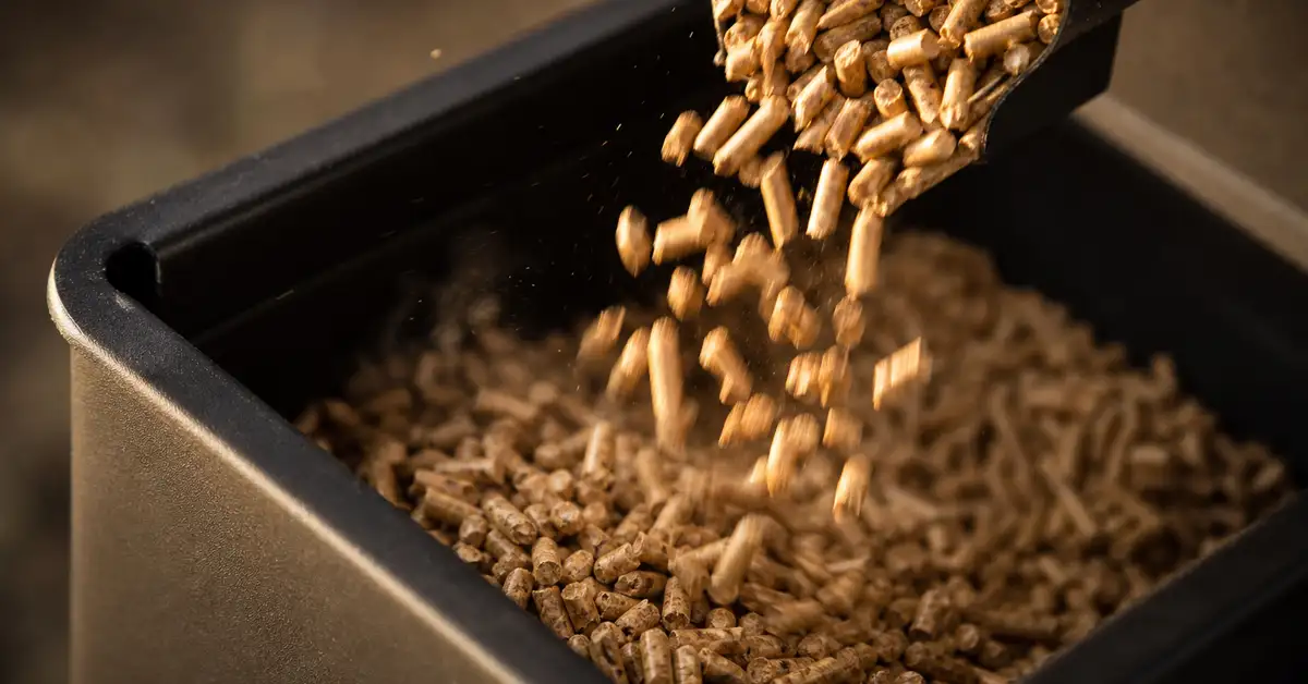 Golden hardwood smoking pellets pouring into a matte black pellet grill hopper