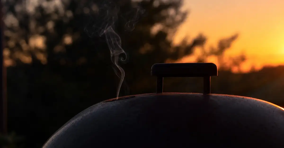 Smoke curling from a closed grill lid at dusk, representing smokers