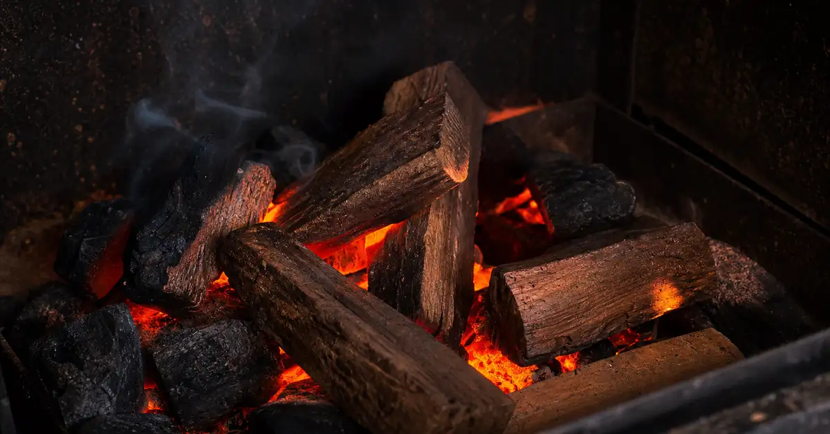 Wood chunks nestled among glowing charcoal embers in a smoker firebox with warm ember glow