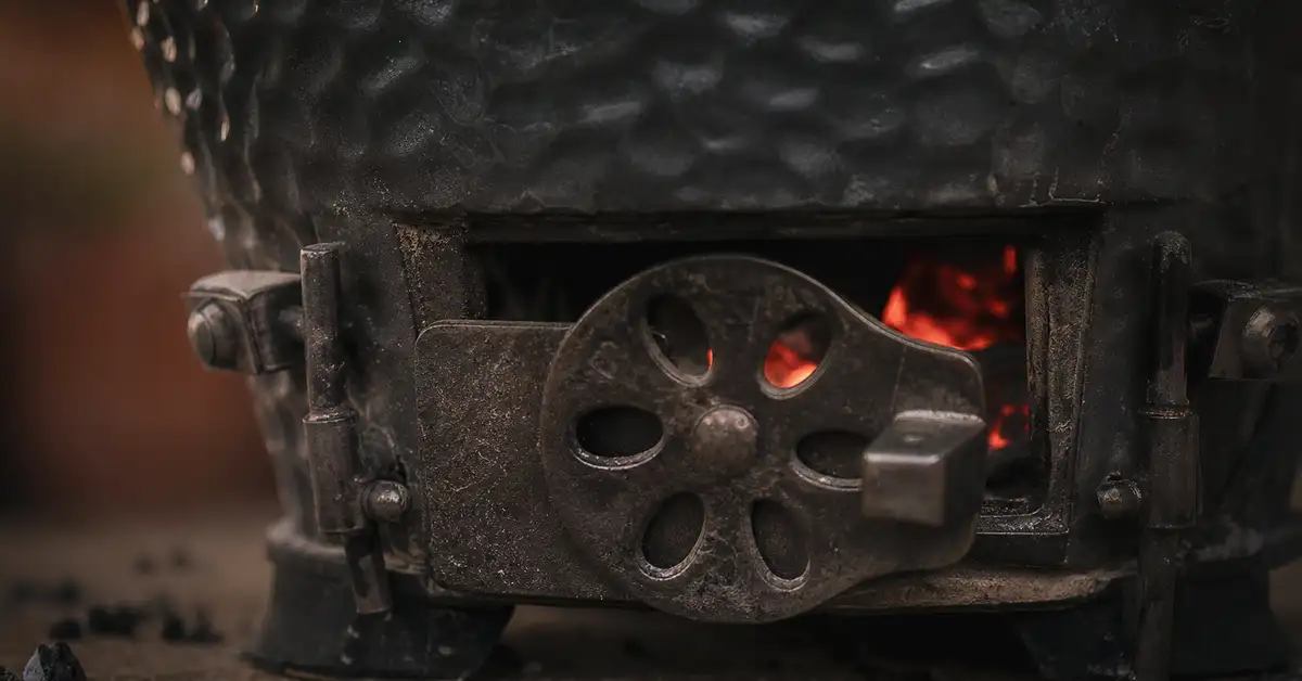 Close-up of a kamado grill's bottom air vent glowing with warm ember light against dark ceramic