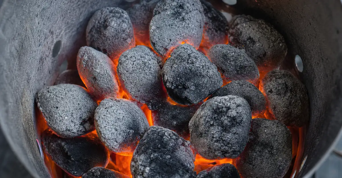 Close-up of charcoal briquettes ashing over inside a chimney starter, glowing orange embers turning gray