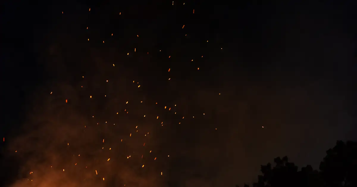 Sparks and glowing embers drifting upward against a dark night backyard sky