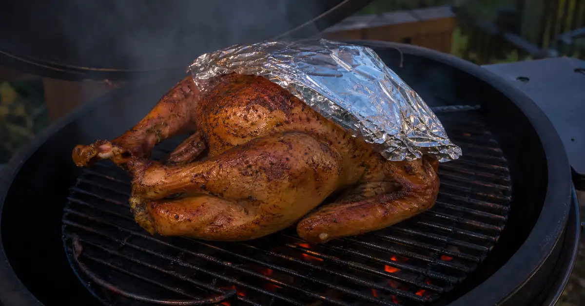 A whole turkey on a smoker grate with the breast loosely tented in foil to slow browning